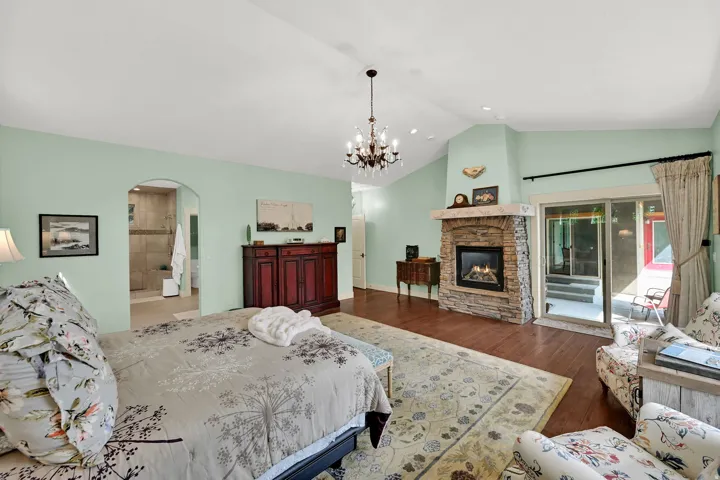 Vaulted ceiling with chandelier, stone-faced fireplace with wood mantel, and sliding glass door to outdoor space