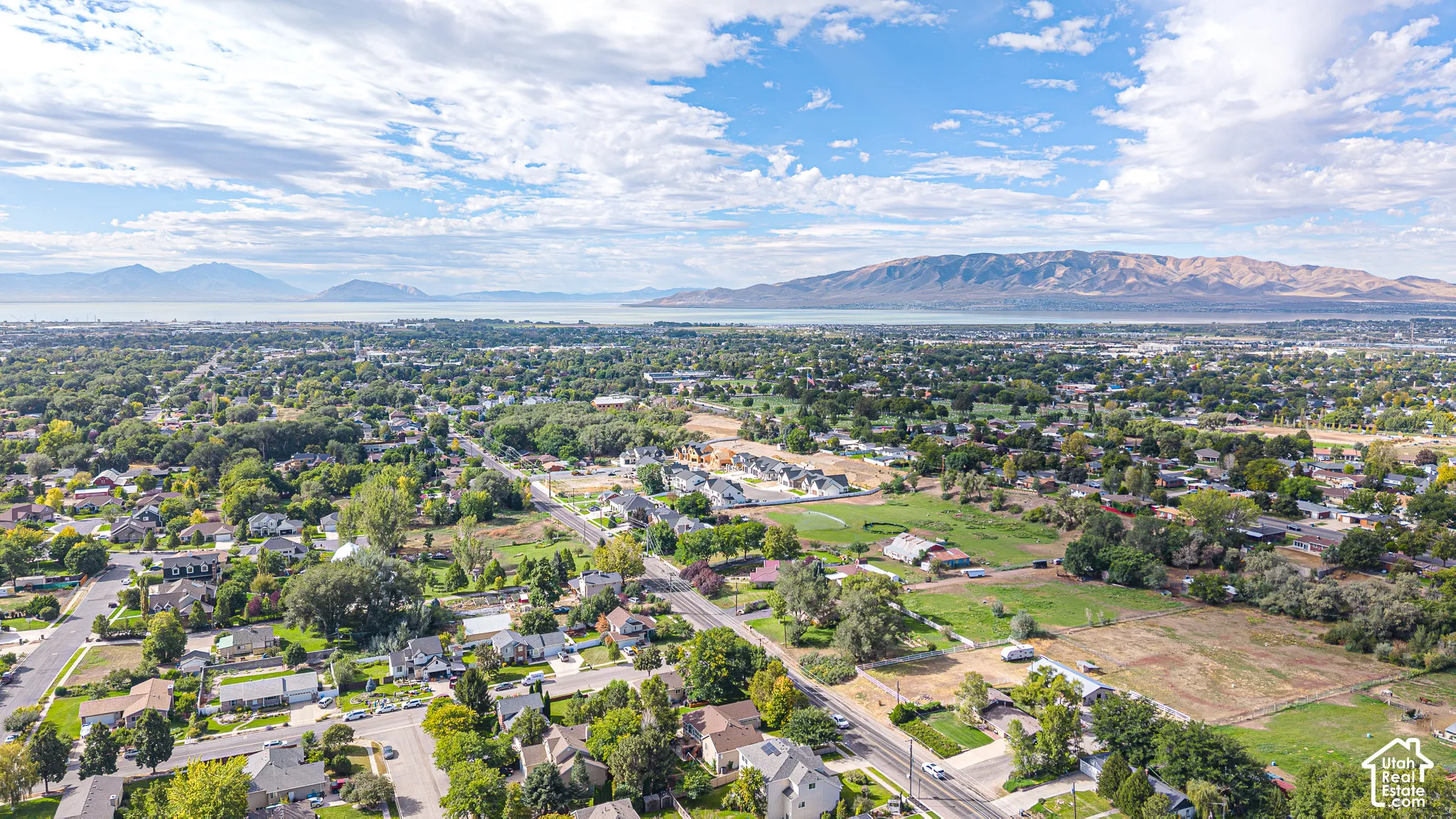 Expansive aerial perspective showcasing a residential area, extensive green landscaping, and distant bodies of water with mountainous backdrops