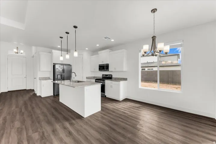 Kitchen with wood-finish flooring, white cabinetry, a central island with a sink, stainless steel appliances, and pendant lighting