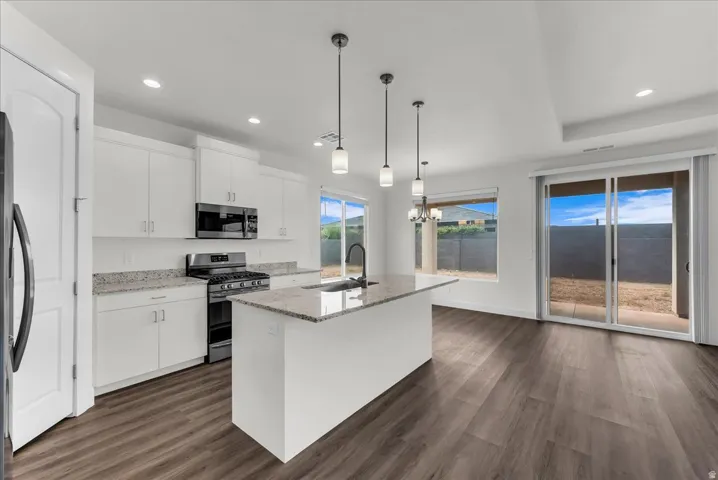 Kitchen and dining space featuring wood-finish flooring, white cabinetry, a kitchen island with stone countertops, stainless steel appliances, and a glass sliding door