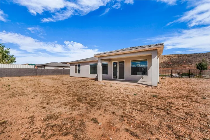 Rear exterior with an extended concrete patio, sliding glass doors, multiple windows, and a walled perimeter