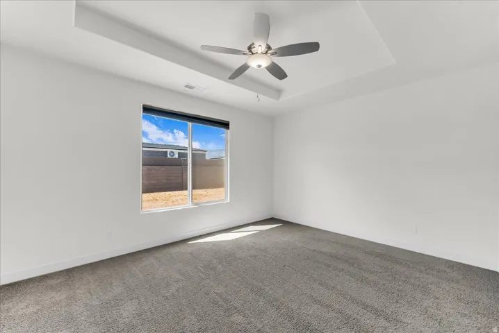 Recessed ceiling with an attached ceiling fan, large window, and gray carpeting