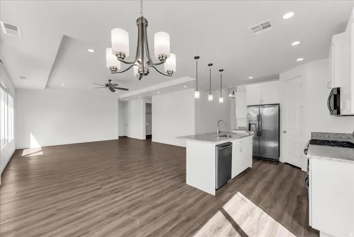 Open-concept living space featuring wood-finish flooring, a tray ceiling, and an integrated kitchen with a center island, stainless steel appliances, and pendant lighting