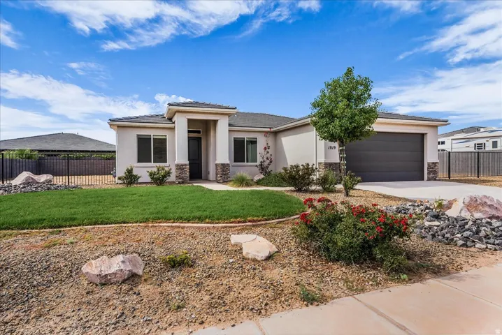 Contemporary stucco exterior with stone accents, a dark garage door, a paved driveway, a manicured lawn, and low-maintenance landscaping