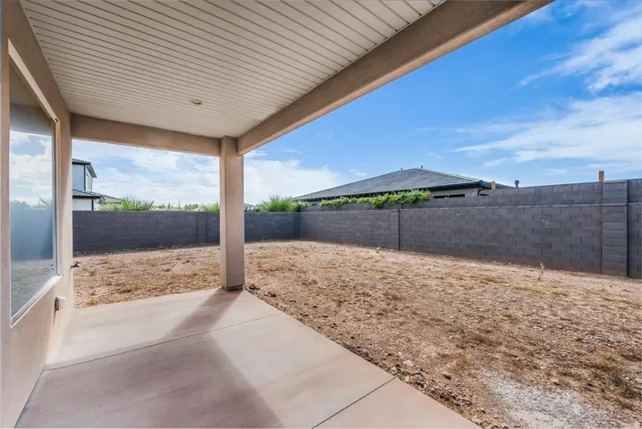 Covered patio with concrete flooring, supported by stucco-finished columns, overlooking a fully-fenced backyard with block wall construction