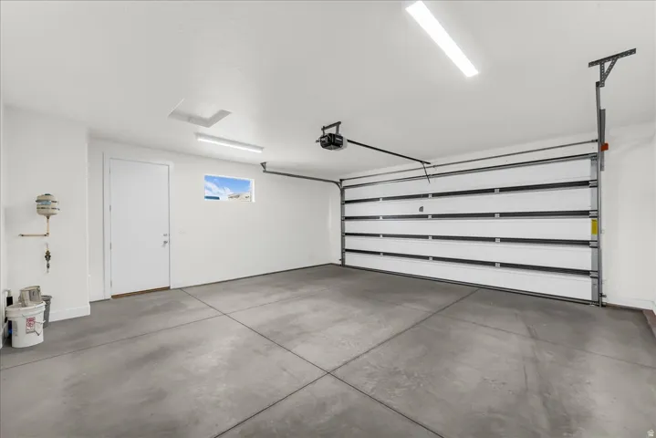 Concrete flooring, white walls, overhead lighting, automated garage door, and a single window