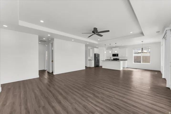 Expansive open-concept living area featuring wood-finish flooring, recessed lighting, and a tray ceiling with a ceiling fan