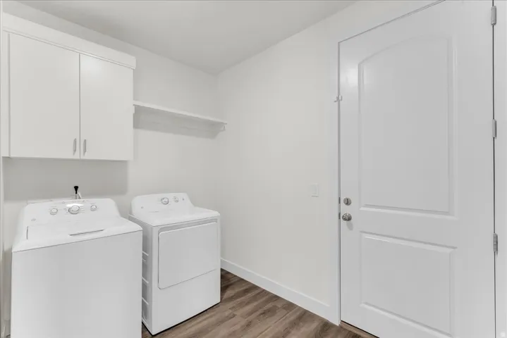 Laundry area featuring wood-finish flooring, white cabinetry, and a storage shelf