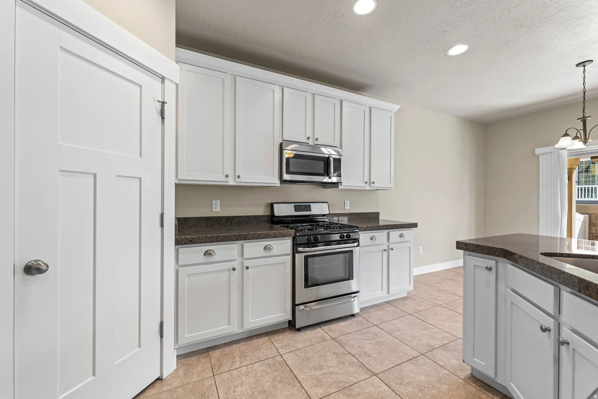 White cabinetry, stainless steel appliances, dark countertops, tiled flooring, and recessed lighting