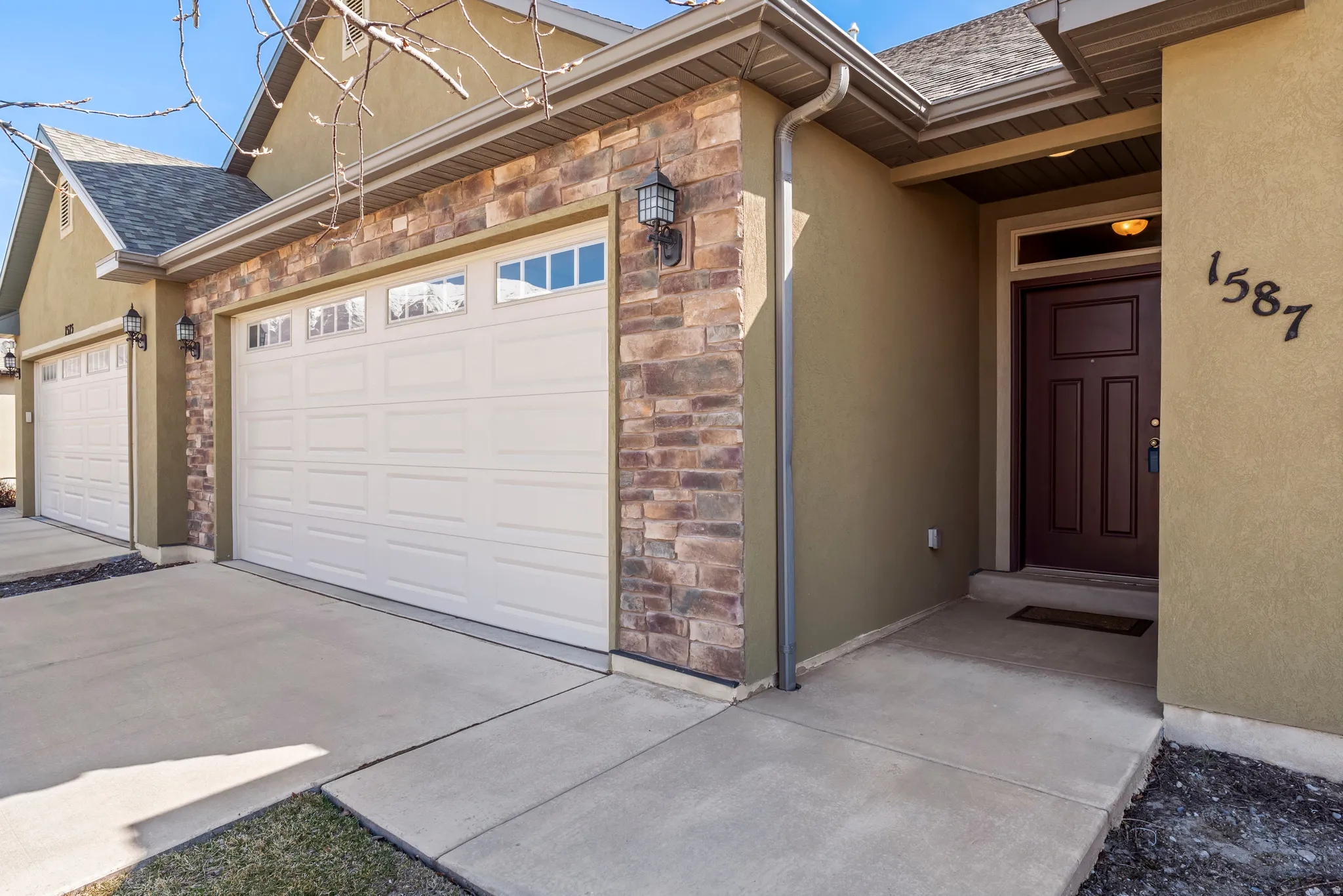 Stucco exterior with stone accent, concrete driveway and walkway, and a dark wood-paneled entry door