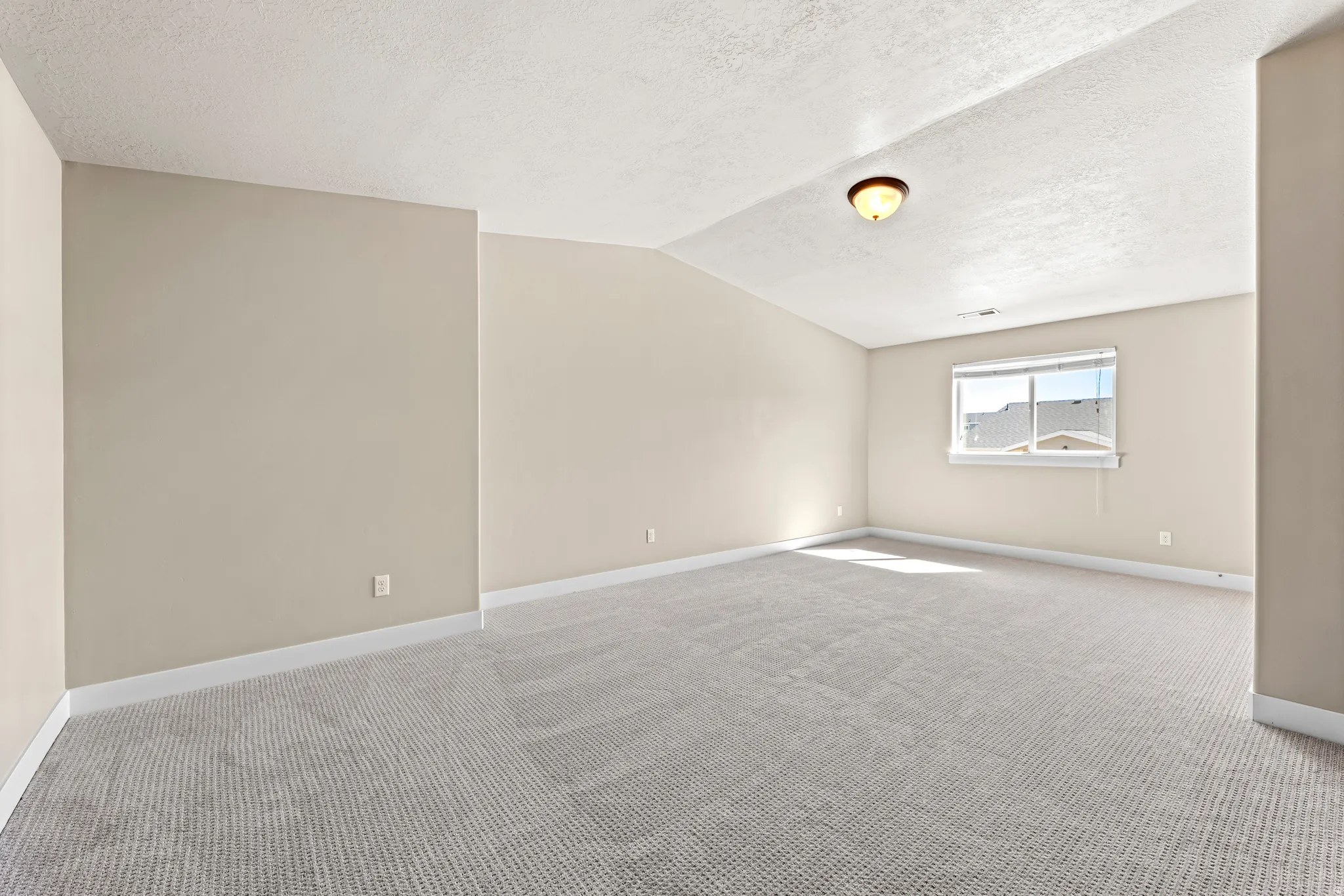 Spacious room featuring neutral paint, textured ceiling, carpeting, and a window with blinds