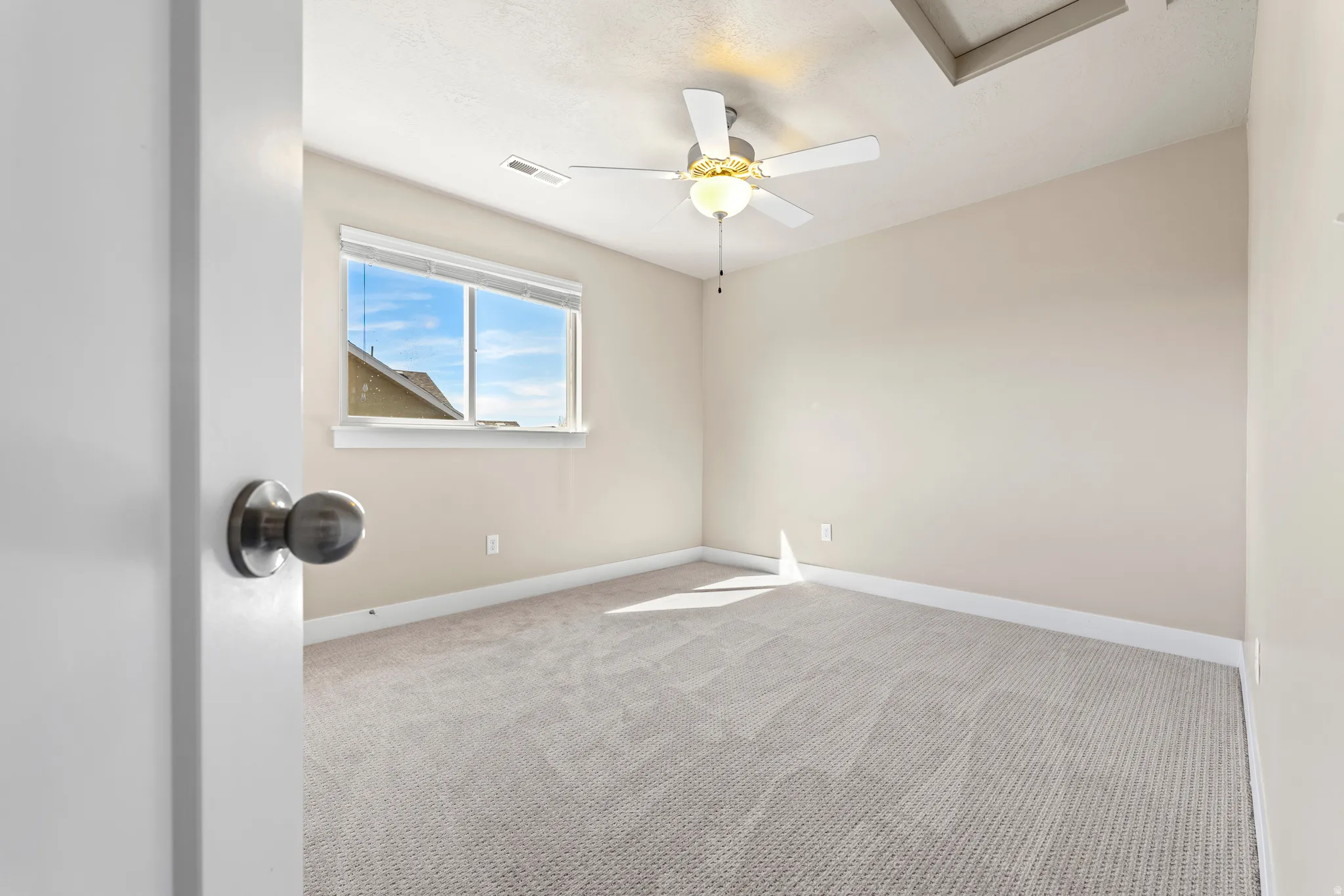 Recessed window with white trim, light neutral wall paint, textured neutral carpeting, ceiling fan with integrated lighting, and a dark bronze door handle