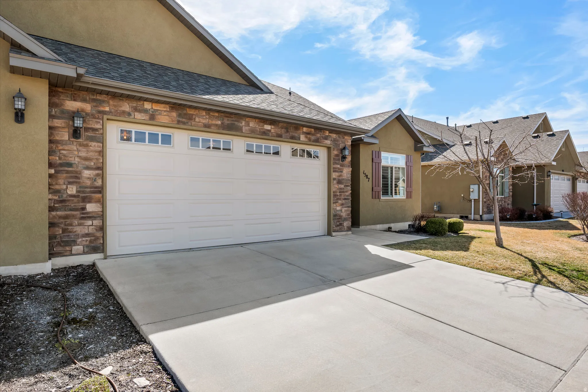 Attached garage with stone veneer accents, concrete driveway, and exterior wall sconces