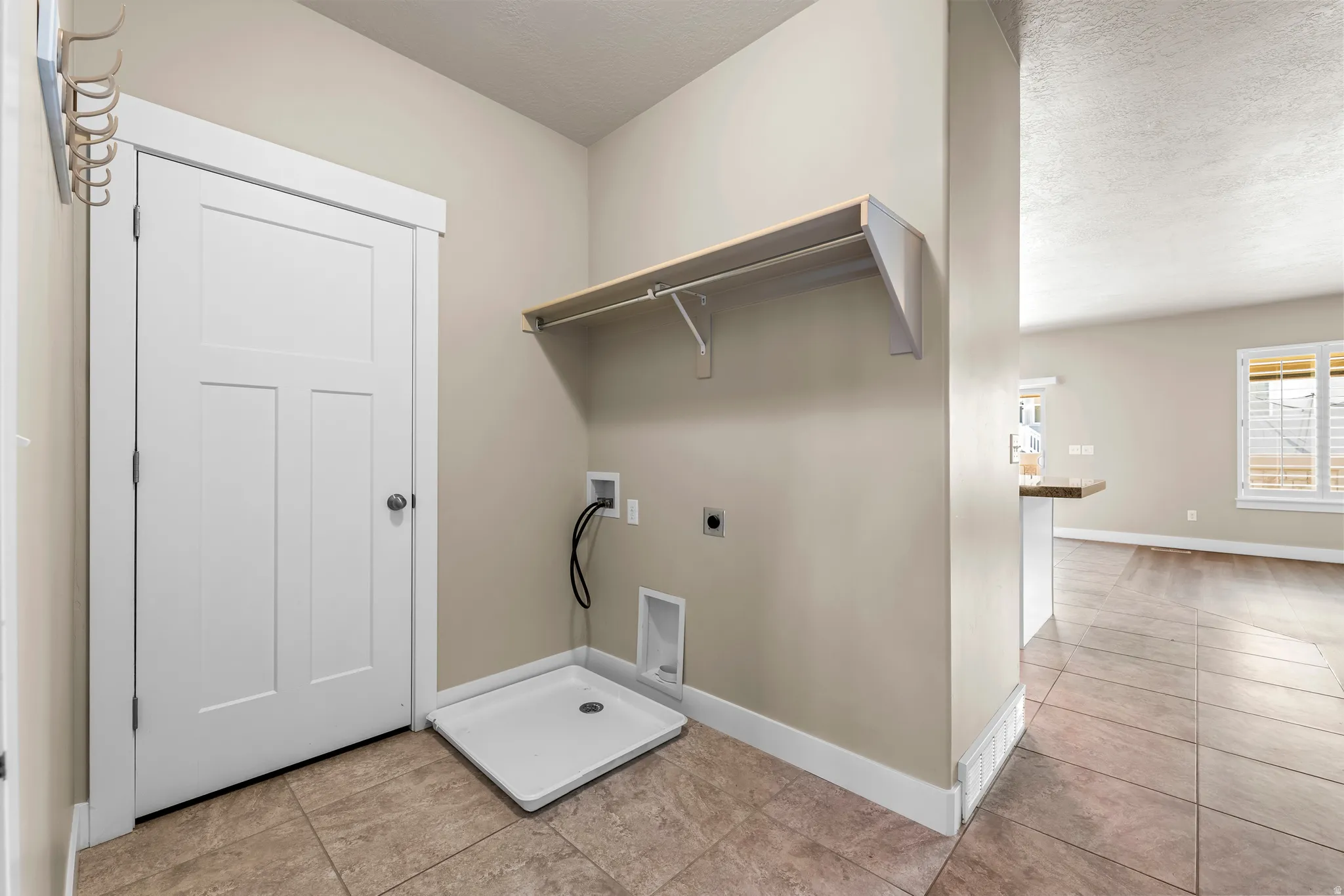 Utility area featuring tile flooring, a pre-plumbed appliance bay, an overhead shelf, a white paneled door, and neutral wall tones