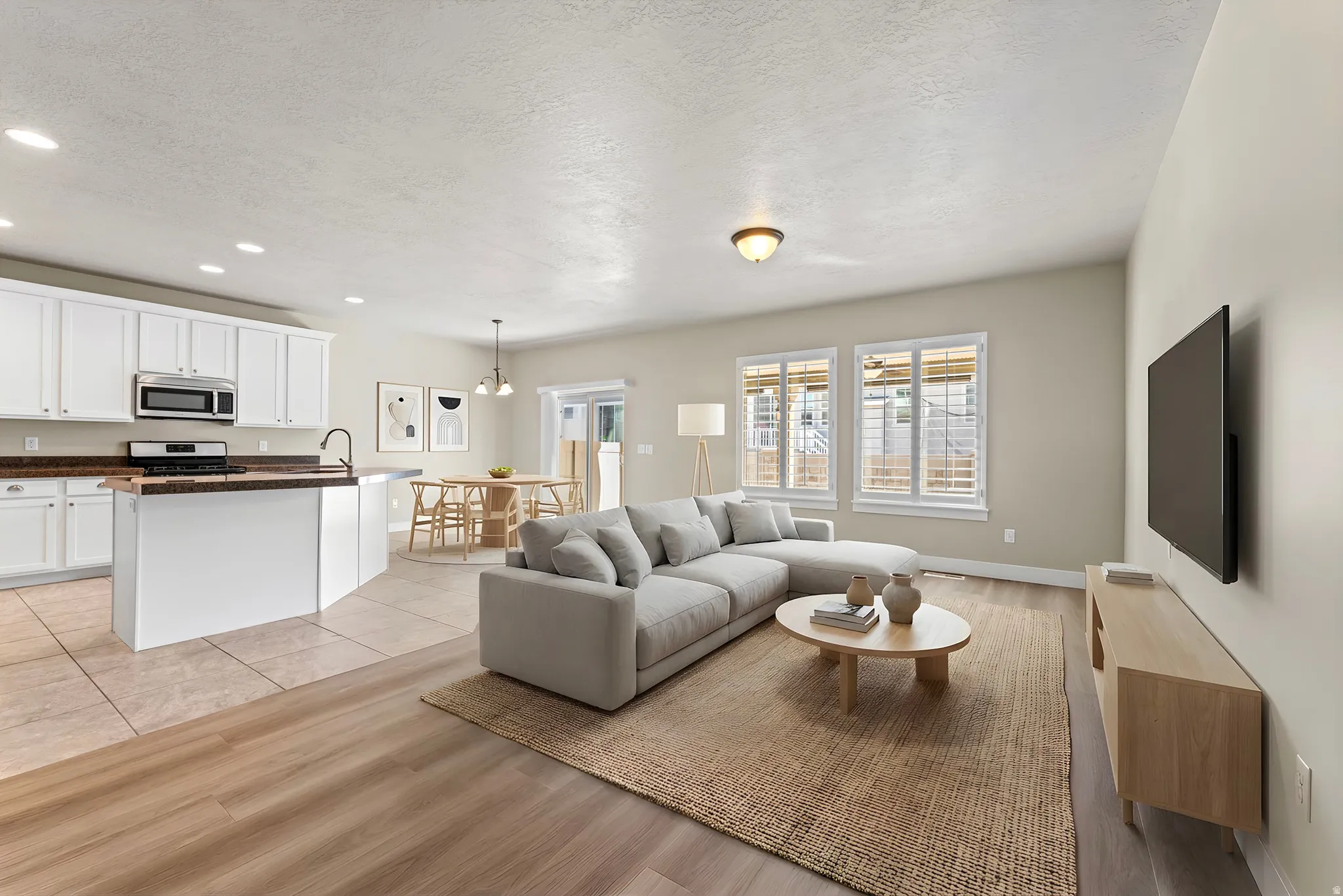Open-concept living area with wood-finish flooring, white cabinetry, dark countertops, and stainless steel appliances
