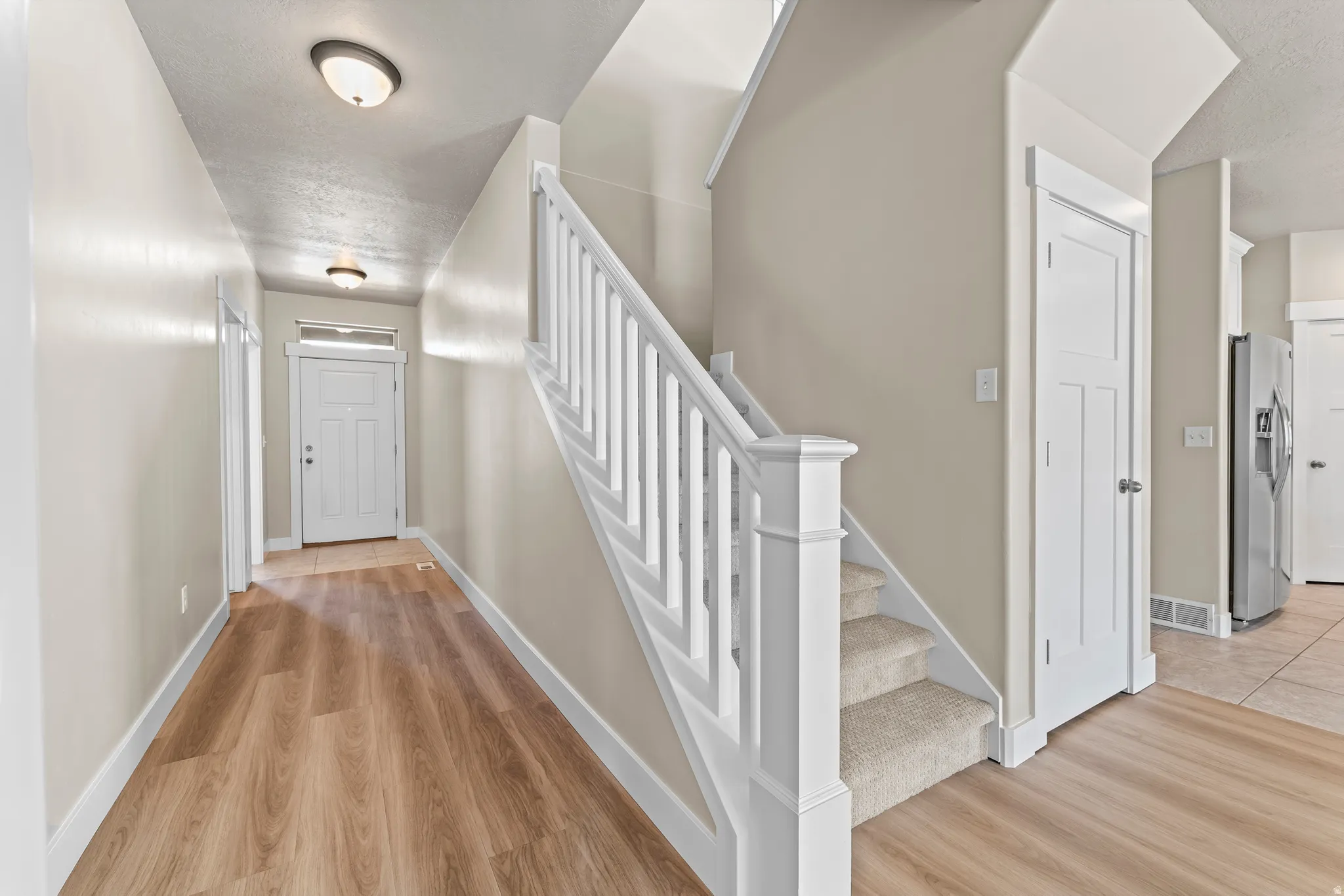 Entryway featuring wood-finish flooring, white paneled doors, a white staircase with carpeted treads, and flush mount lighting