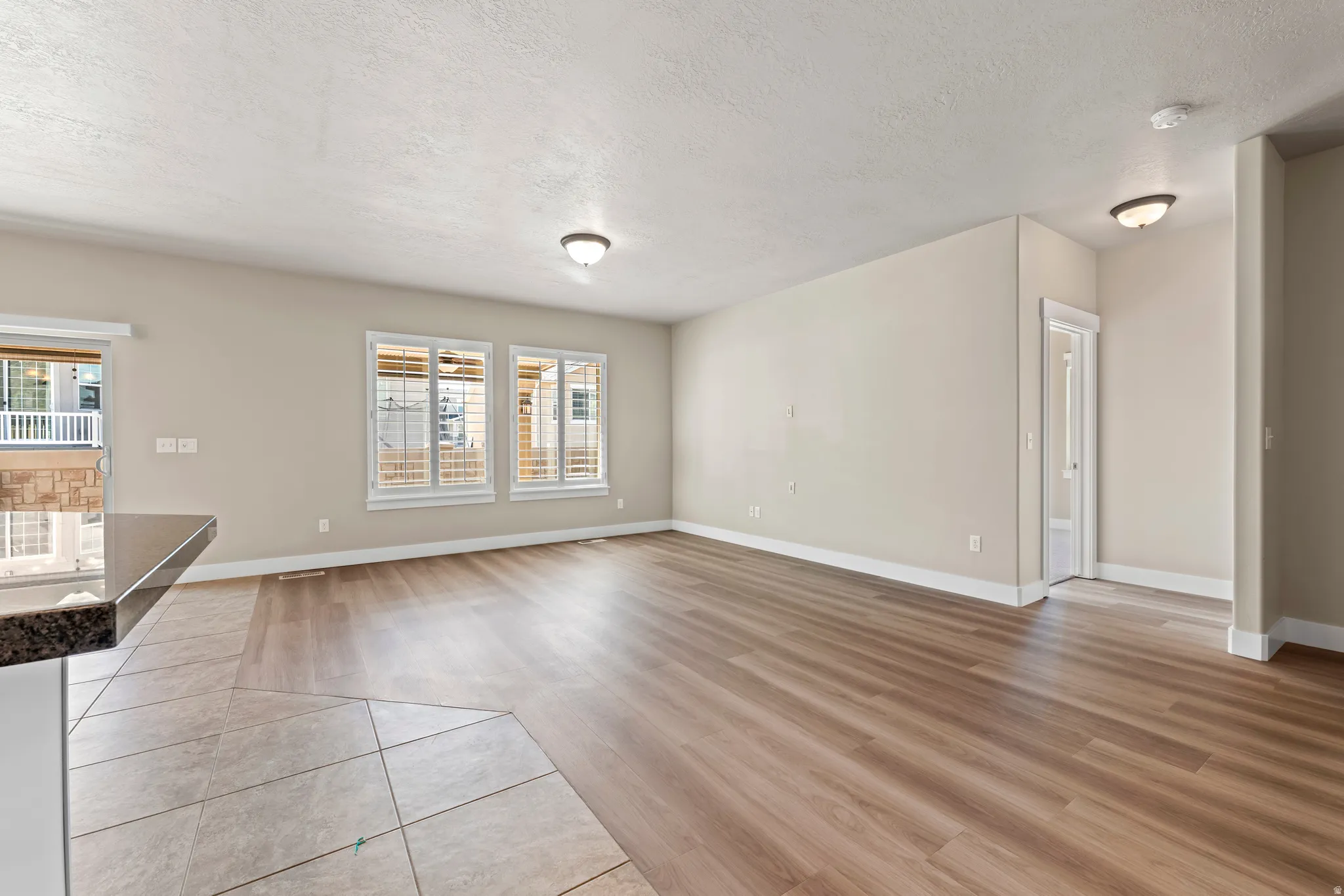 Wood-finish flooring throughout, complemented by a tiled entry, multiple windows with blinds, and flush-mount ceiling lights