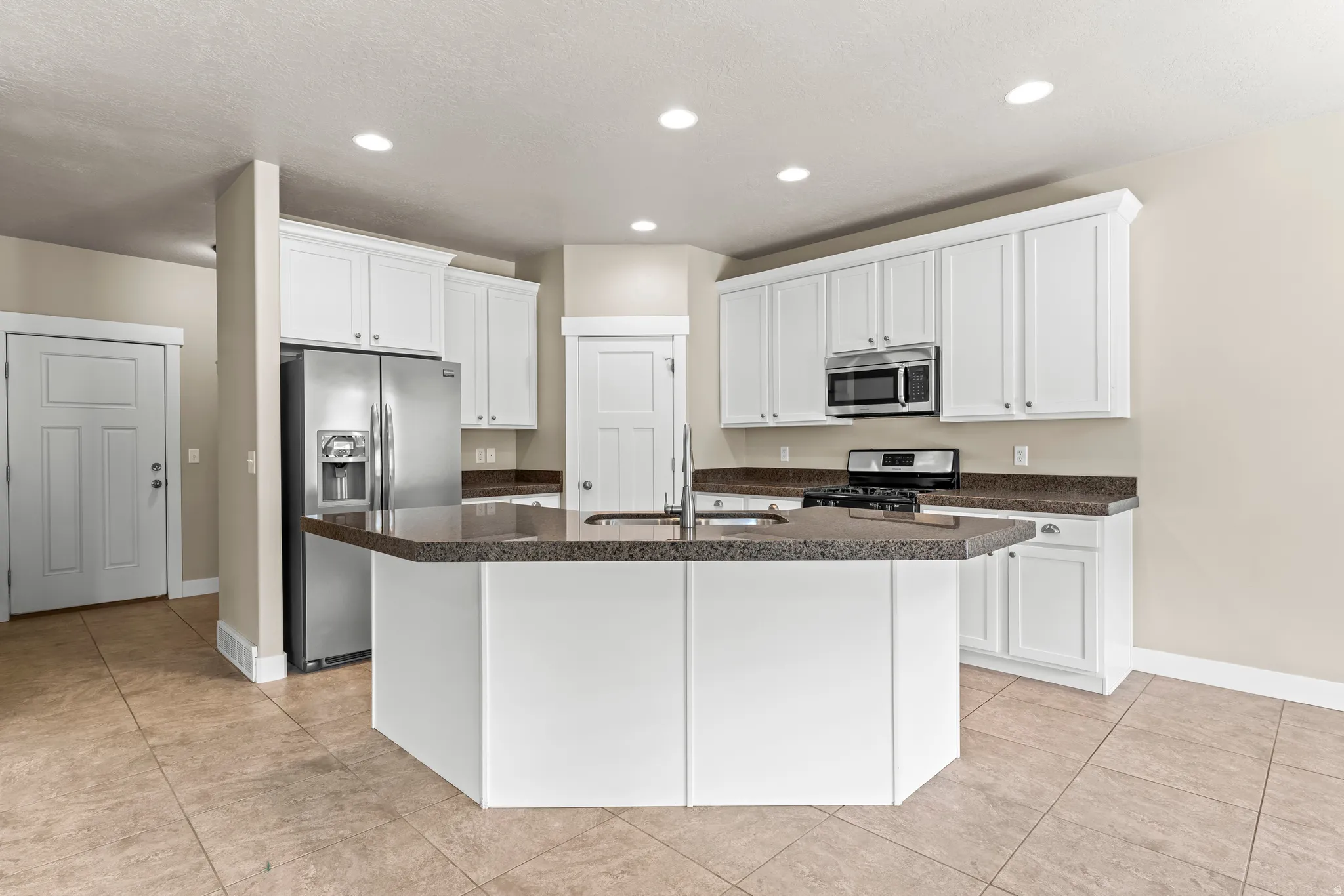 Kitchen featuring white cabinetry, stainless steel appliances, a center island with a sink, stone countertops, and tiled flooring