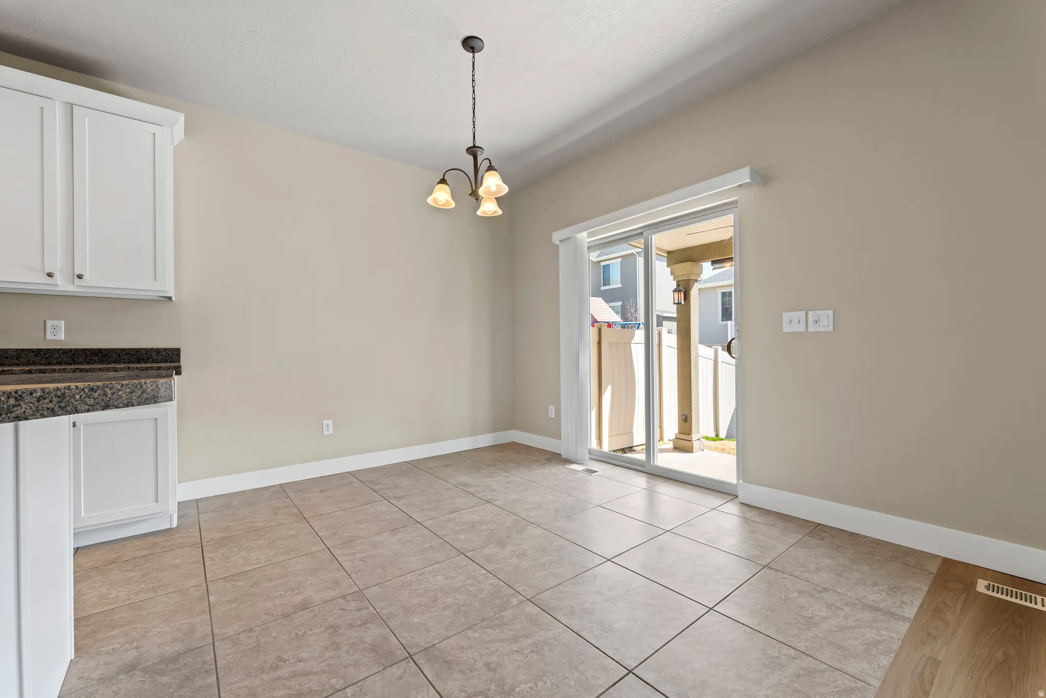 White cabinetry with dark countertops, tile flooring, vaulted ceiling, and sliding glass door