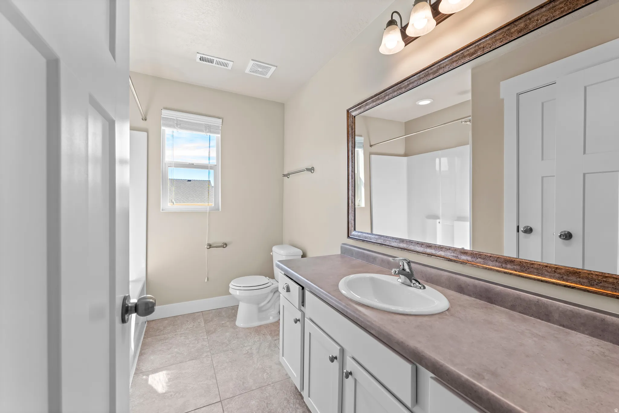 Vanity with integrated sink, expansive mirror, tile flooring, built-in cabinetry, and window with blinds