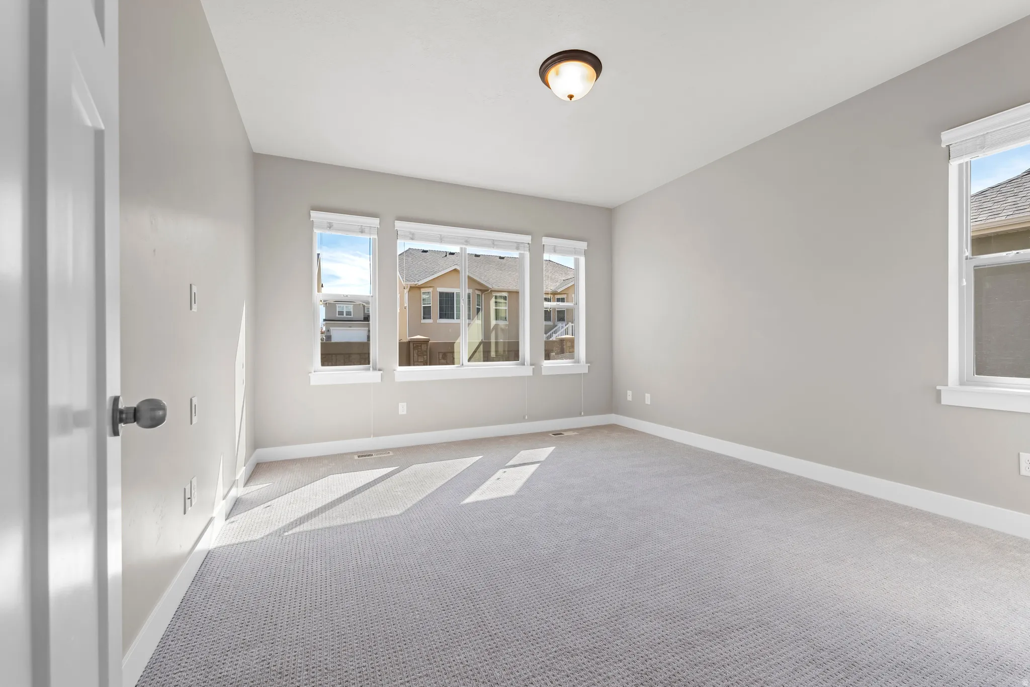 Recessed ceiling light fixture, three large windows, light grey wall paint, white trim, and carpet flooring