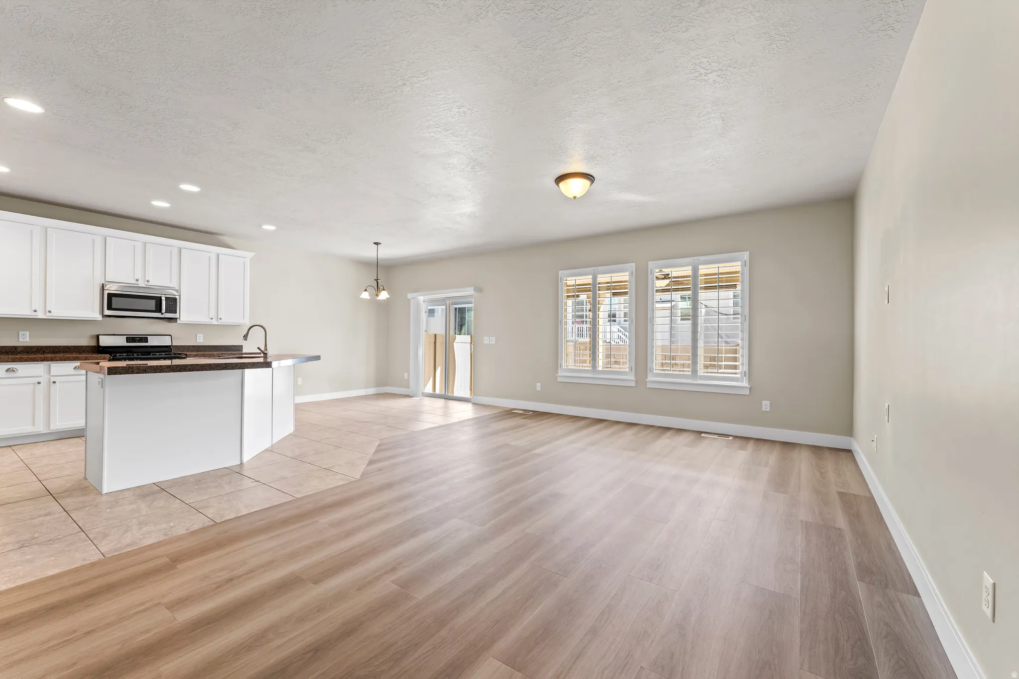 Open-concept living area with wood-finish flooring, white cabinetry, a kitchen island, stainless steel microwave, and sliding glass door