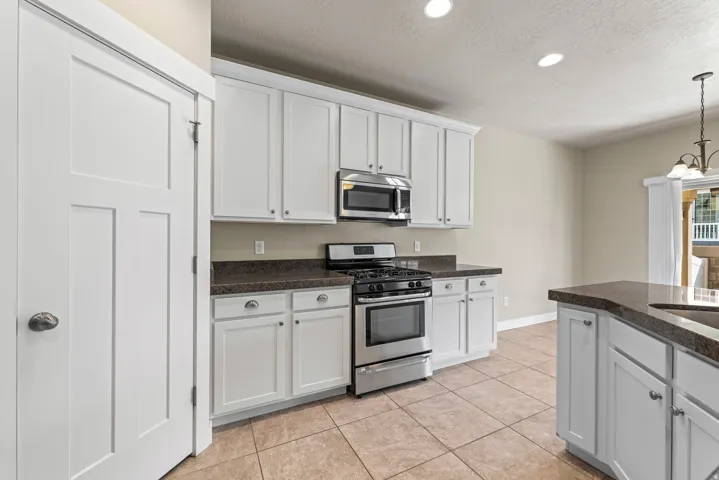White cabinetry, stainless steel appliances, dark countertops, tiled flooring, and recessed lighting