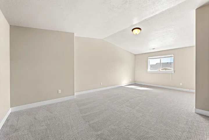 Spacious room featuring neutral paint, textured ceiling, carpeting, and a window with blinds