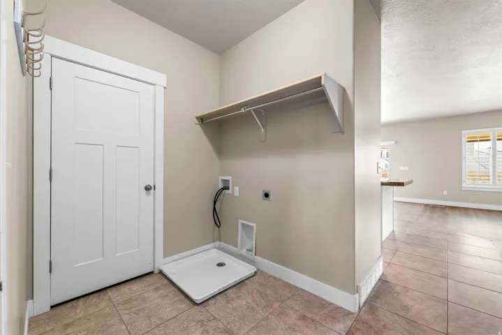 Utility area featuring tile flooring, a pre-plumbed appliance bay, an overhead shelf, a white paneled door, and neutral wall tones
