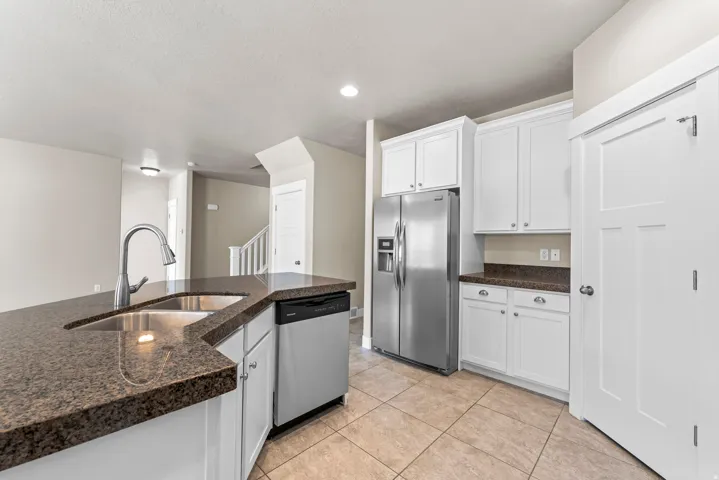 Kitchen featuring white cabinetry, stone countertops, stainless steel appliances, and tile flooring