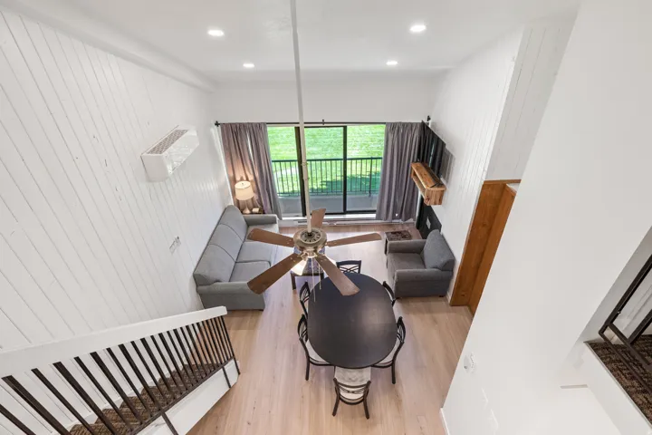 Vaulted ceiling, ceiling fan, wood-finish flooring, white shiplap-style wall paneling, and sliding glass doors