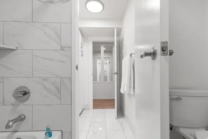White subway tile shower surround with chrome fixtures, white square floor tiles, and a built-in toilet