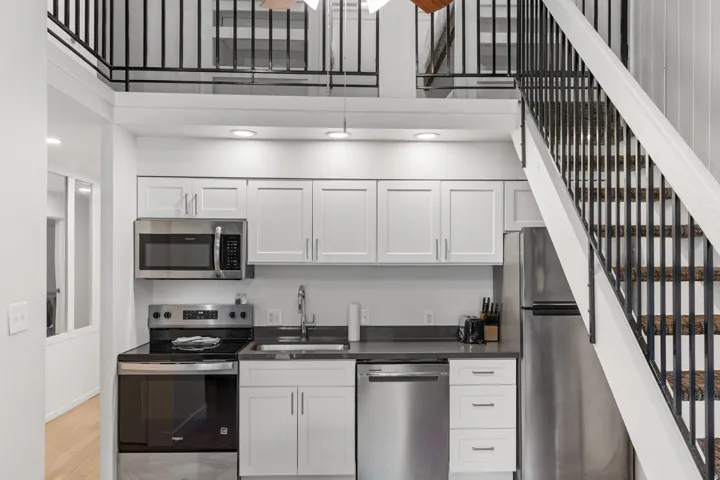 Compact kitchen featuring stainless steel appliances, white cabinetry, dark countertops, and recessed lighting