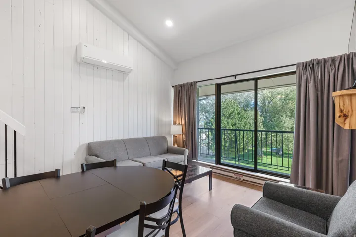 Sliding glass doors opening to a private balcony, wood-finish flooring, white vertical wall paneling, and a built-in wall-mounted air conditioning unit