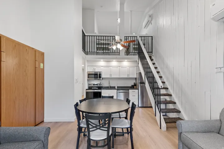 Loft-style architecture with an open-concept layout, wood-finish flooring, a kitchen featuring stainless steel appliances, and a staircase with a black metal railing