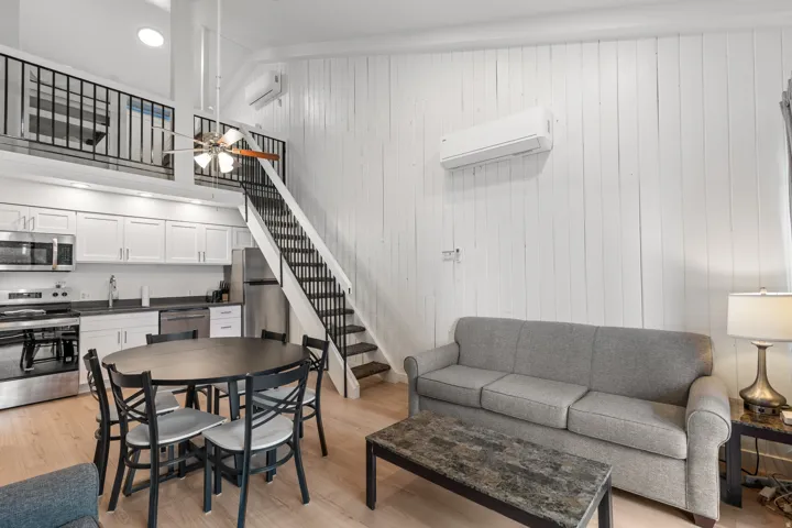 Open-concept living area with light wood-finish flooring, white shiplap walls, and a high vaulted ceiling