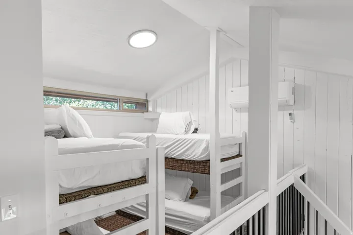 White bunk beds with integrated storage, wood-paneled walls, and a recessed ceiling light