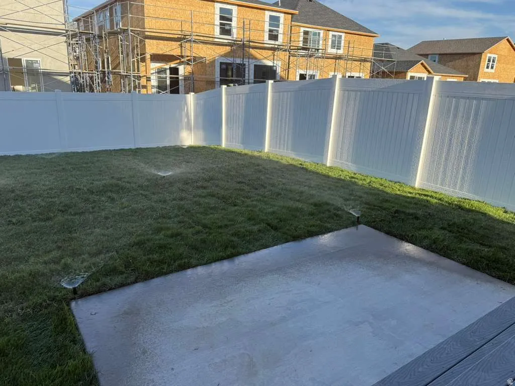 Manicured lawn with an integrated sprinkler system, a concrete patio, and a white privacy fence