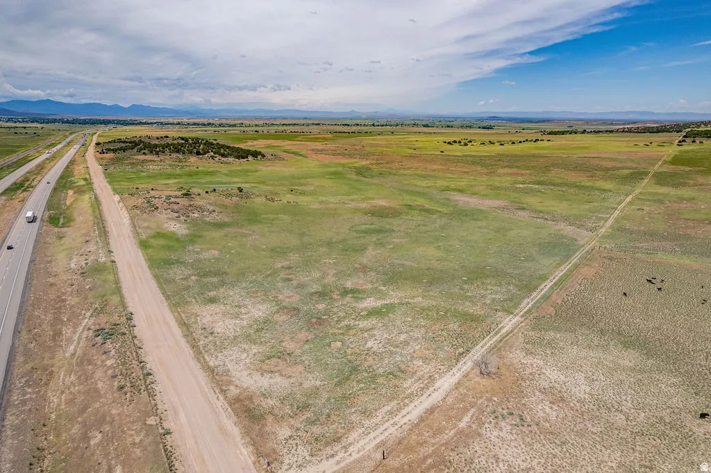 Expansive open land featuring a dirt road, adjacent paved highway, and distant mountain range