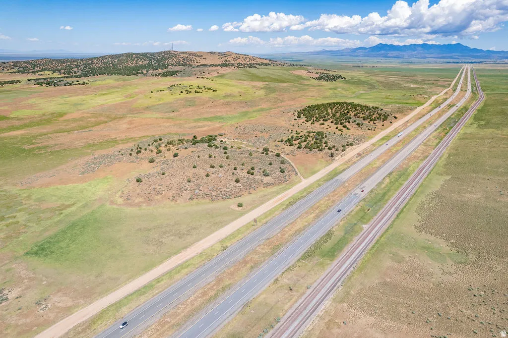 Expansive land parcel featuring open fields, distant mountains, and direct access to a multi-lane highway and railway