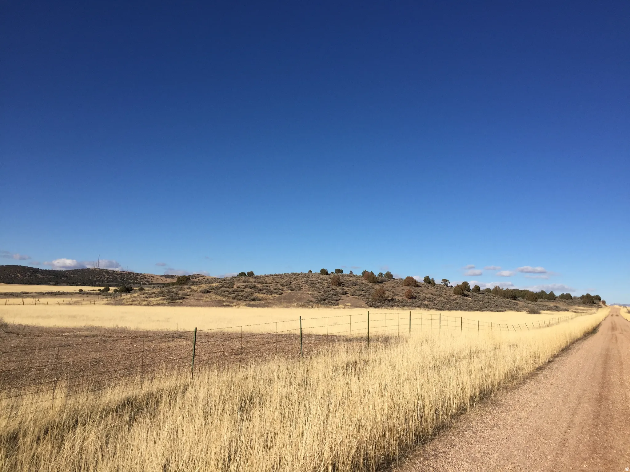 Expansive rural landscape featuring a dirt road, open fields, and distant hills
