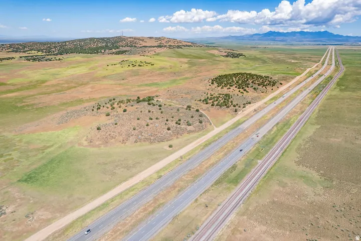 Expansive land parcel featuring open fields, distant mountains, and direct access to a multi-lane highway and railway