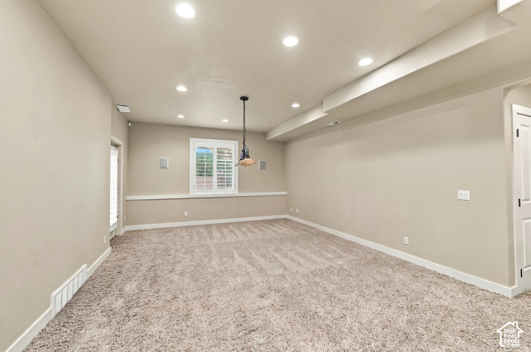 Recessed ceiling lighting, a decorative pendant light, white window shutters, and plush carpeting