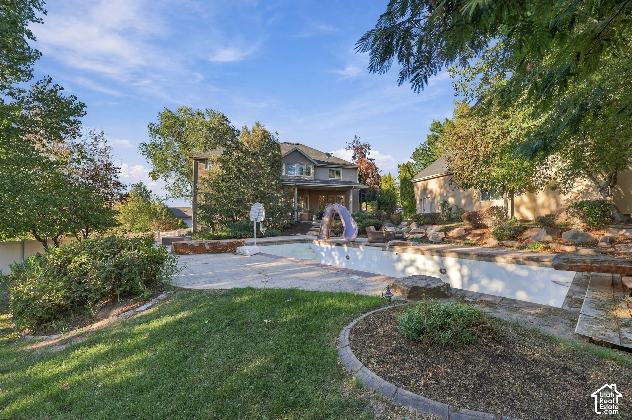Expansive backyard with a large inground pool, mature trees, landscaped rock features, and a spacious lawn area