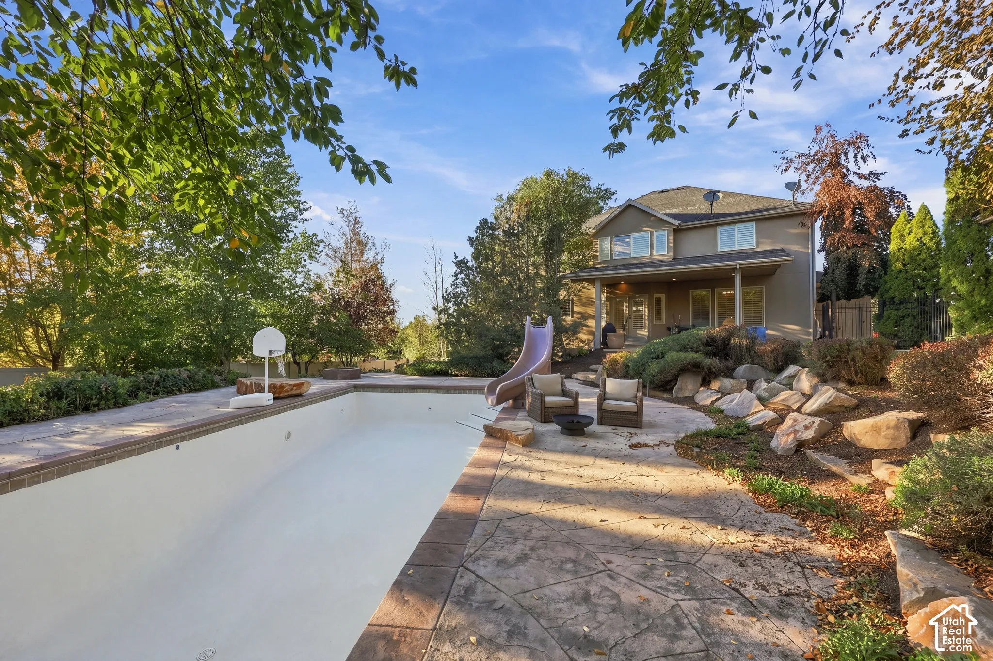 Two-story exterior with a covered patio, featuring an in-ground pool with a surrounding hardscape and a rock garden