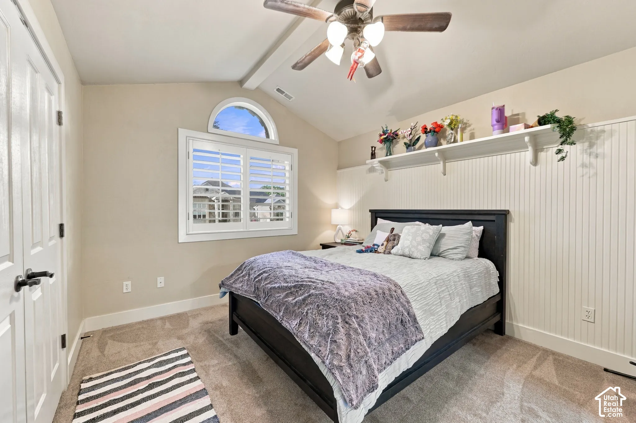 Vaulted ceiling with a ceiling fan, arched window with plantation shutters, beadboard wall paneling, built-in wall shelf, and carpeted flooring