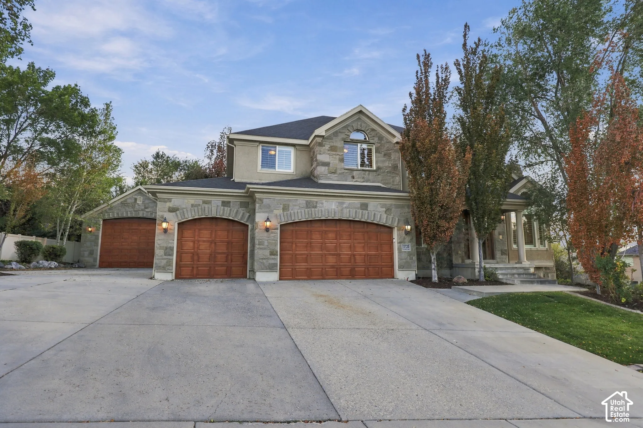 Stone facade architecture with arched garage doors, concrete driveway, and mature landscaping