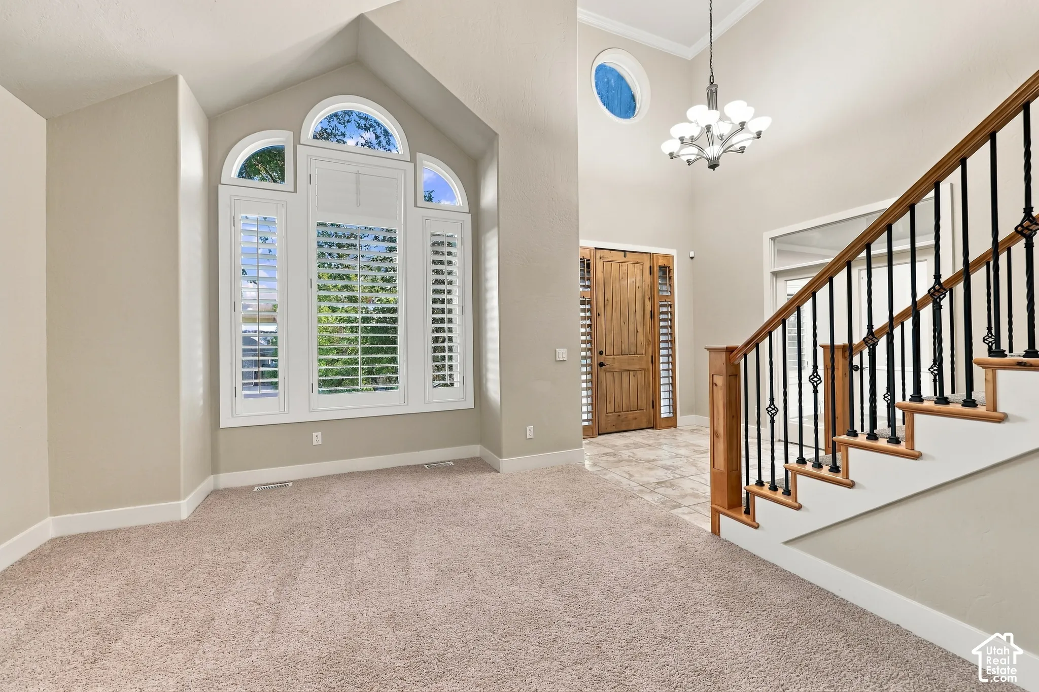 Two-story foyer featuring a chandelier, a natural wood entry door with sidelights, and a staircase with wood treads and wrought iron spindles