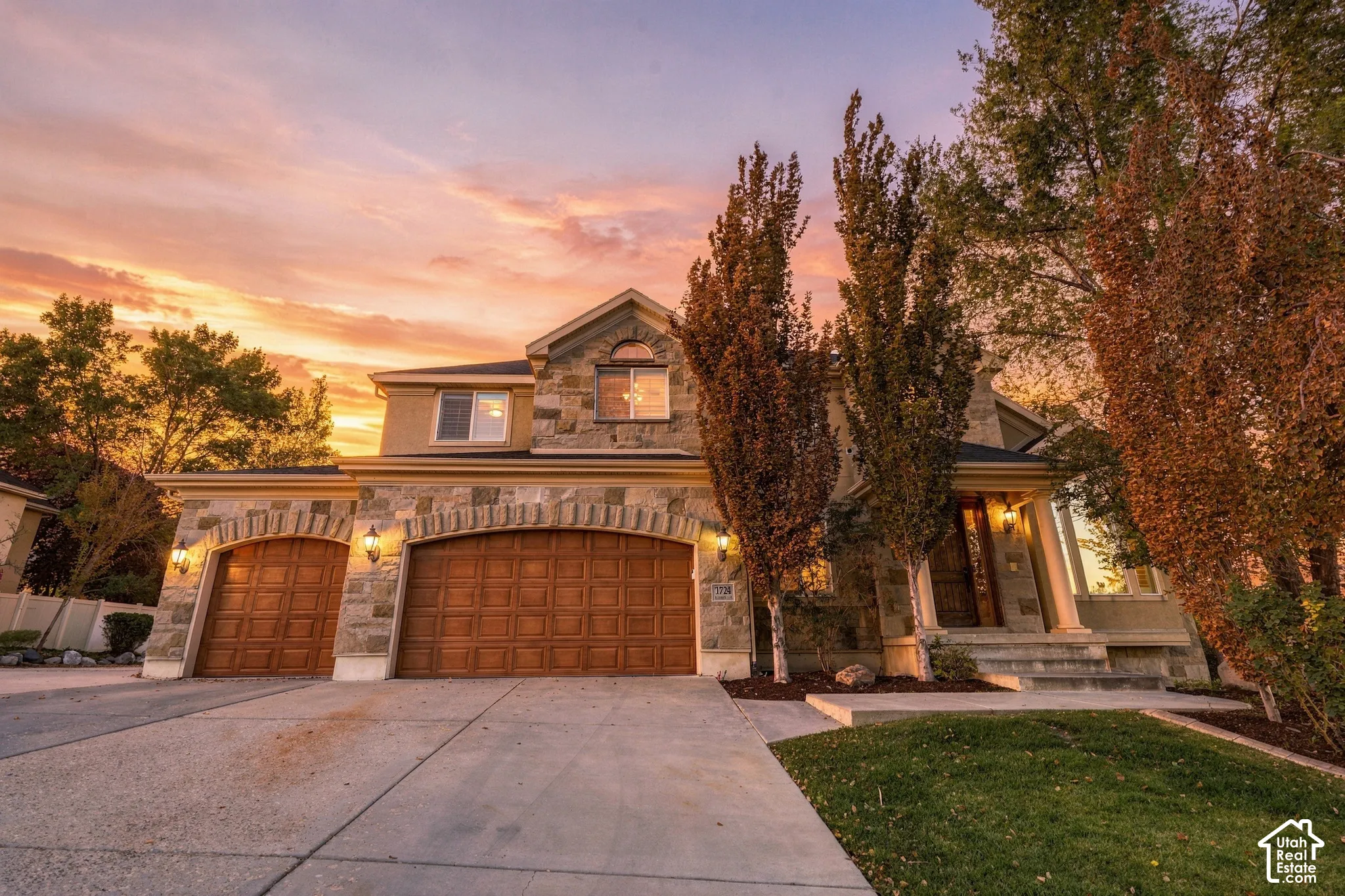 Stone and stucco exterior with arched garage doors, concrete driveway, front entry with columns, and mature landscaping