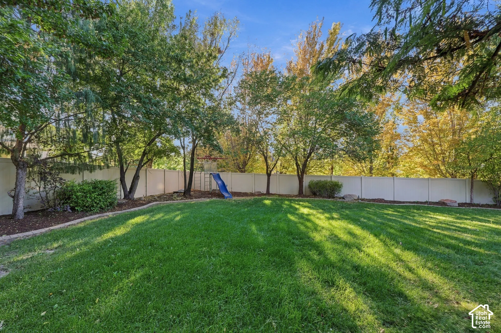 Expansive green lawn with mature trees and a privacy fence